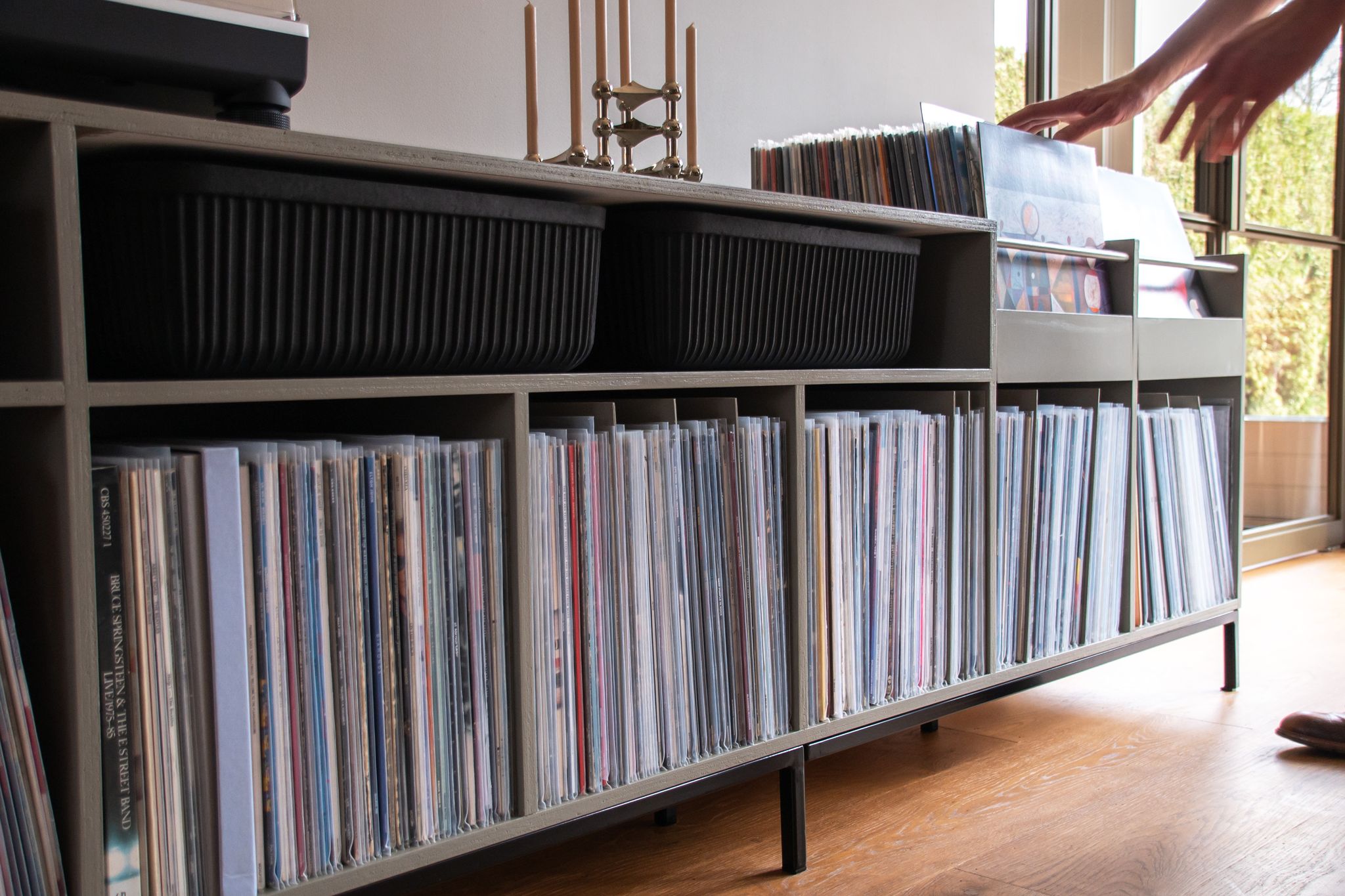 Donkere platenkast met vinylplaten rechtop in vakken, doorbladerbakken en ruimte voor een platenspeler.
